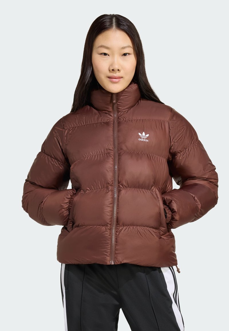 Brun pufferjakke med høj krave, lynlåslukning, elastiske manchetter og lommer foran. Har hvidt Adidas-logo på brystet.