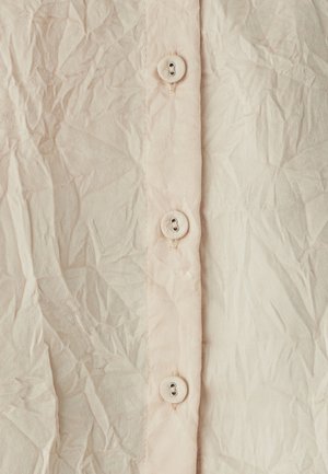Tissu froissé rose clair avec une rangée verticale de quatre boutons ronds, présentant une surface texturée et des plis visibles.
