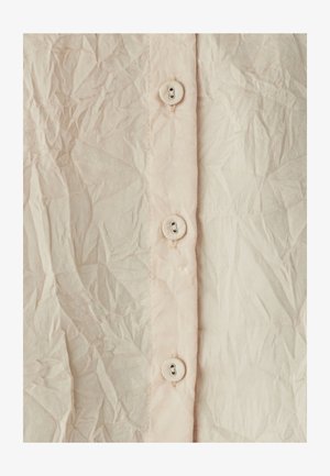 Svetlo roza gubana tkanina z navpičnim stolpcem štirih okroglih gumbov, ki ima teksturirano površino in vidne gube.