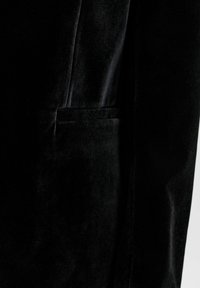 Melnā samta žakete ar šaura piegriezuma, ar vērtām atloku un krūšu kabatu. Tekstūra izskatās maiga ar nelielu spīdumu.