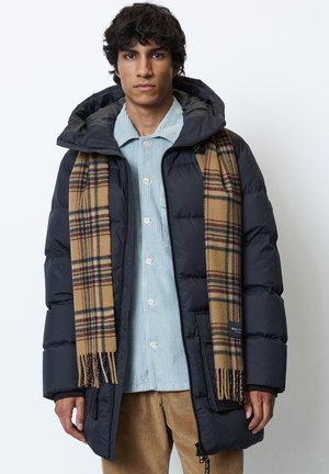 Marineblauer Pufferjacke mit Kapuze, kombiniert mit einem braunen karierten Schal. Die Jacke verfügt über einen Reißverschluss und eine glänzende, gesteppte Textur. Darunter ein hellblaues Hemd.