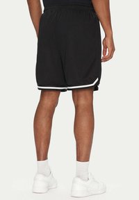 Pantaloni sportivi neri in rete con rifiniture bianche, vita elastica e tasche laterali, abbinati a scarpe da ginnastica bianche e calze di lunghezza media.