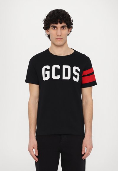 T-shirt noir avec le logo "GCDS" blanc sur le devant, présentant un accent rayé rouge sur la manche gauche. Fabriqué en coton doux.