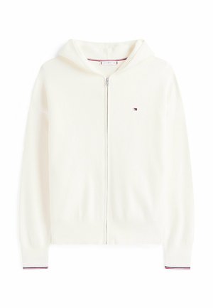 Haut à zip blanc fabriqué en tissu doux, avec une capuche spacieuse, des poignets côtelés avec des rayures rouges et bleues, et un petit logo sur la poitrine.