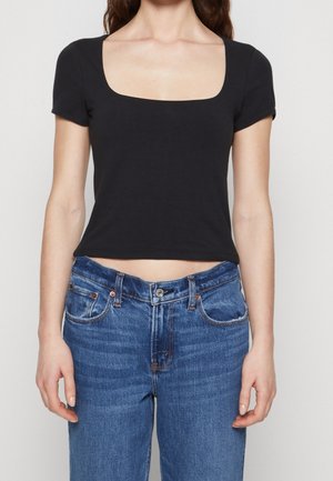 Sort tætsiddende crop top med firkantet udskæring og korte ærmer, parret med mid-rise blå denim jeans med forlommer og en klassisk knap.