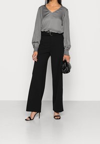 Blusa grigia setosa con scollatura a V e maniche lunghe gatherate, abbinata a pantaloni neri a vita alta e ampia gamba, e sandali con tacco aperti neri.