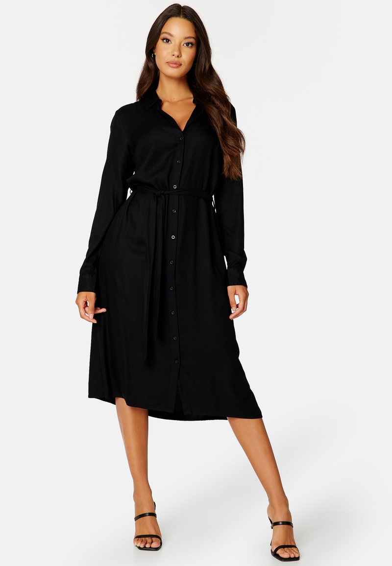 Vestito camicia lungo nero con maniche lunghe realizzato in tessuto morbido, dotato di bottoni sulla parte anteriore e vita aderente con una cintura abbinata.