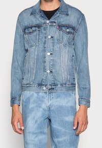 Jasnoniebieska kurtka dżinsowa z guzikami na przodzie, dwiema kieszeniami na piersi oraz kieszeniami bocznymi. Posiada klasyczne szwy i lekko zniszczoną teksturę.