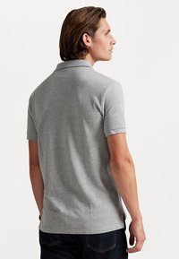 Camisa polo gris de manga corta, con un cuello clásico, un tejido texturizado y aberturas laterales en el dobladillo para mayor facilidad de movimiento.