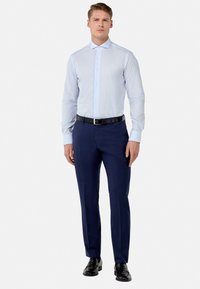 Lichtblauw gestreept overhemd met lange mouwen, met knoopsluiting bij de kraag, gecombineerd met donkerblauwe broek en zwarte leren schoenen.