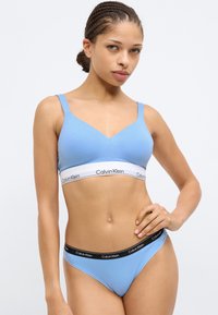 Ανοιχτό μπλε βαμβακερό σουτιέν bralette με σχέδιο V-neck και ρυθμιζόμενους ιμάντες. Διαθέτει λευκή ταινία με το λογότυπο "Calvin Klein". Περιλαμβάνεται ταιριαστό μπλε στρινγκ.