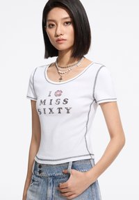 Tricou alb ajustat cu mânecă scurtă, având un print grafic texturat "ÎMI ESTE DOR DE ȘAISPREZECE" în litere închise și un imprimeu cu buze. Cusături în contrast.