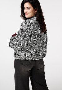 Zwart-witte jas met zebrapatroon en textuur, met kraag en een afgeronde zoom, gecombineerd met donkergrijze spijkerbroek. Geen opvallende hardware zichtbaar.