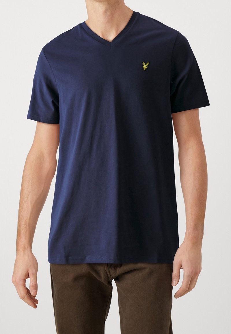 Marineblaue Baumwoll-T-Shirt mit kurzen Ärmeln, V-Ausschnitt-Design, ausgestattet mit einem kleinen grünen Emblem auf der Brust und einer glatten, einfarbigen Textur.