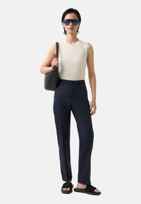 Krémový top bez rukávů, námořnické kalhoty na míru, černé sandály a oversized sluneční brýle. Modelka drží šedou texturovanou kabelku.