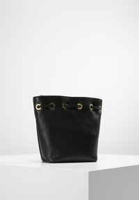 Svart läder bucket bag med guldfärgade öglor och dragsko-stängning. Slät textur och strukturerad form.