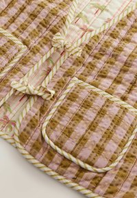 Robe en coton matelassé avec un motif rayé marron et rose, dotée de finitions rayées et de petits nœuds décoratifs sur les poches. Texture douce, broderie détaillée.