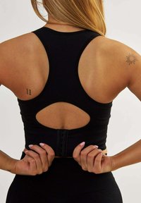 Czarny stanik sportowy z wyścigowymi plecami, z wycięciem z tyłu i zapięciem na haczyk, wykonany z teksturowanej tkaniny.