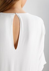 Vestido blanco con un escote redondo y un detalle de apertura en la parte posterior con un botón, en una tela suave y lisa, con mangas cortas.