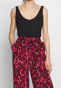 Un débardeur noir à encolure en V profonde, associé à un pantalon ample avec un motif léopard rouge et noir.