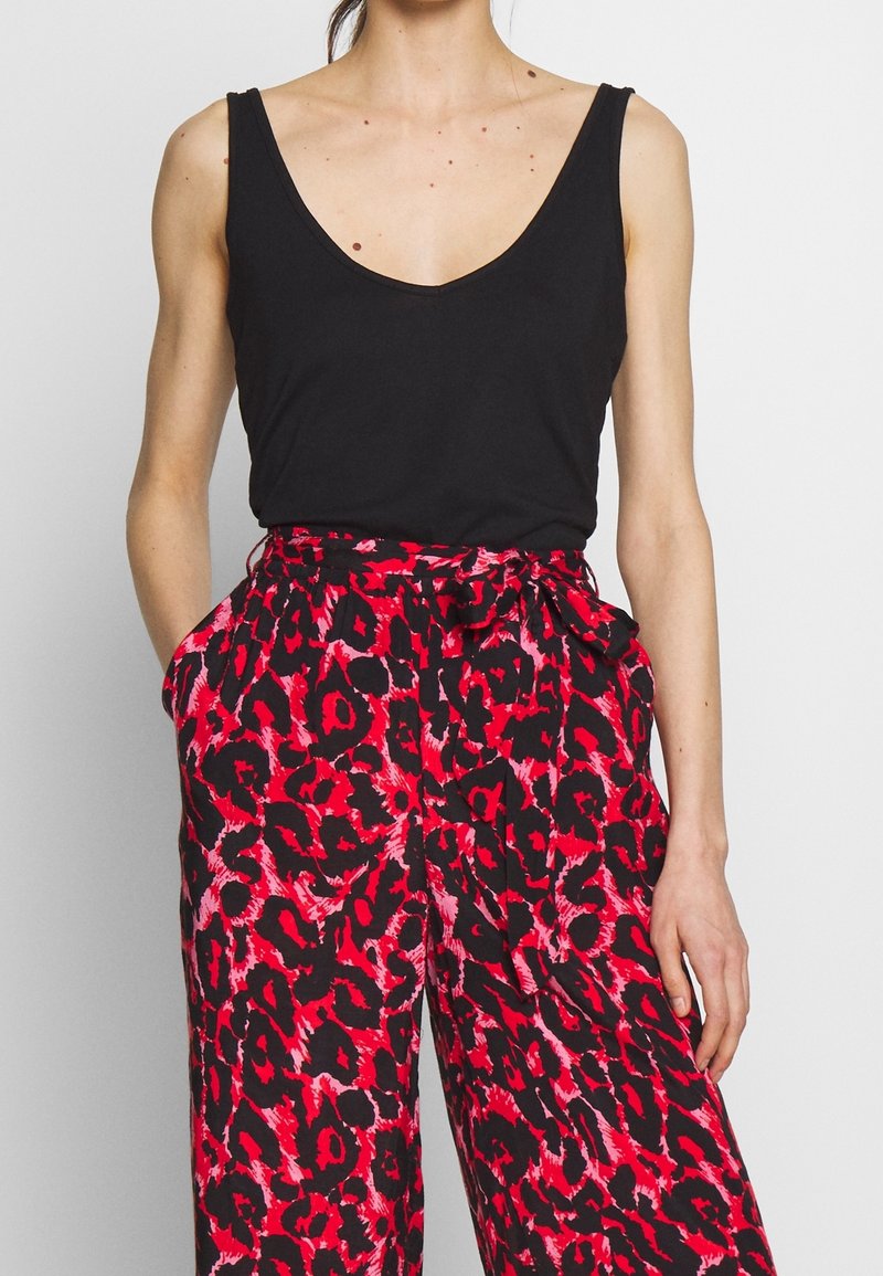 Un débardeur noir à encolure en V profonde, associé à un pantalon ample avec un motif léopard rouge et noir.