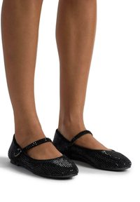 Zapatos planos negros con una superficie texturizada y brillante, con suela plana y una correa decorativa con hebilla a través del empeine.