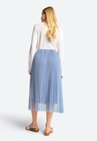 Lyseblå, plisseret midiskirt med en blød, gennemsigtig tekstur. Elastisk talje, parret med en lysefarvet langærmet top og afslappet fodtøj.