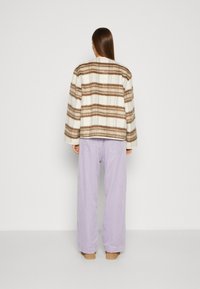 Ullete rutetejakke med brune og kremfargede striper, kombinert med lyse lavendel vide bukser. Teksturerte, oversized design med senkede skuldre.