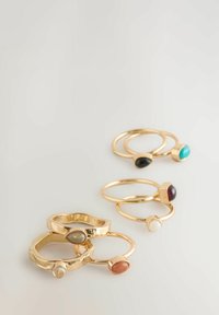 Set aus sechs goldenen Ringen mit verschiedenen Edelsteinakzenten, darunter Türkis, schwarze, rote und weiße Steine, die unterschiedliche Formen und Texturen aufweisen.