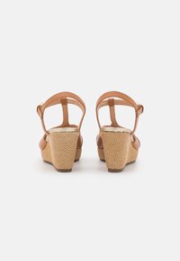 Sandales compensées en cuir marron avec un talon tissé texturé, une sangle réglable et une section de orteils lisse. Design simple et fonctionnel.