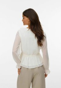 Hvit, gjennomsiktig bluse med peplum-liv og lange, utblåste ermer. Glatt tekstur og delikate rynkede detaljer ved ermene.