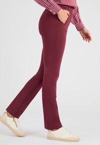 Pantalones burdeos hechos de tela elástica, con un diseño ajustado, bolsillos laterales y combinados con zapatillas de color claro.