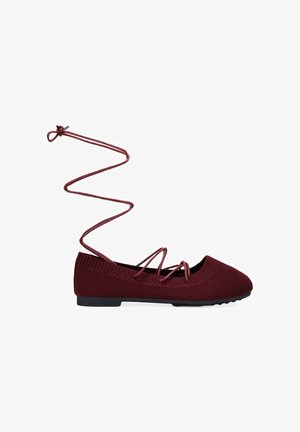 Bailarina de punto color burdeos con tiras cruzadas y largos lazos que se atan alrededor del tobillo, con suela plana negra.