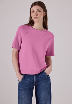Sweatshirt rose à manches courtes avec un col rond, coupe décontractée et texture douce, associé à un jean en denim bleu à jambes larges.