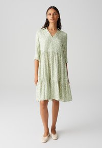 Robe verte à motifs avec un col, décollet�é en V, manches trois-quarts et jupe à volants. Tissu léger avec une texture douce.