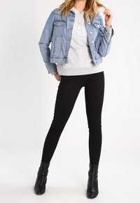 Chaqueta de denim de color azul claro, con un diseño ajustado, dos bolsillos frontales. Sudadera gris con la letra "A", combinada con jeans skinny negros y botas negras.