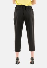 Pantaloni neri, plissettati, con gamba affusolata, vita elastica e due tasche posteriori. Abbinati a tacchi aperti.