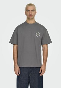 Graues Baumwoll-T-Shirt mit kurzen Ärmeln und Rundhalsausschnitt, mit einem kreisförmigen weißen Grafikaufdruck auf der linken Brust.