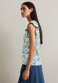 Bloemenpatroon top in groen, blauw en wit; heeft gerimpelde mouwen en een getailleerde silhouet. Gecombineerd met een denim rok.