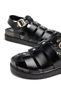Sandalias de cuero negro con múltiples correas, hebilla ajustable, plantilla de corcho texturizado y suela de goma moldeada para agarre.