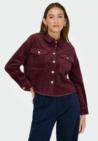 Burgundská kordová zkrácená bunda s knoflíkovou přední částí, dvěma náprsními kapsami a třepeným lemem, se stříbrnými knoflíky a texturovanou látkou.