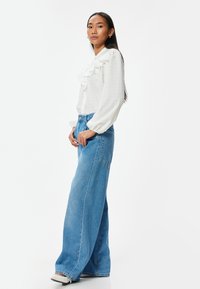 Blusa bianca con un fronte arricciato, tessuto strutturato e maniche lunghe abbinata a jeans in denim blu a vestibilità ampia con vita alta e gambe larghe.