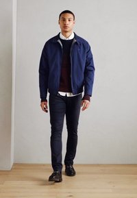 Chaqueta de piloto navy, suéter burdeos, camisa blanca, pantalones ajustados negros, zapatos negros. Textura suave, ajuste casual en un fondo neutro.