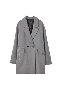Blazer de doble botonadura en un patrón de espiga negro y blanco. Presenta grandes solapas, dos bolsillos frontales y un forro interior suave.