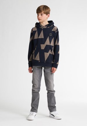 Hoodie marine avec des motifs géométriques beiges, poche avant et capuche avec cordon, associé à un jean gris et des baskets blanches.