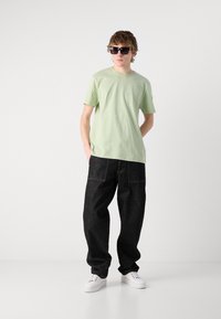 Light green cotton t-shirt, loose-fitting dark denim jeans, white sneakers, and black sunglasses. Simple design with no visible patterns.