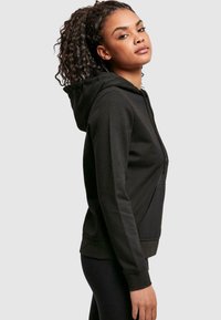 Black hoodie with a front pocket, adjustable drawstring hood, and a soft texture. Fitted design, shown worn with black leggings.