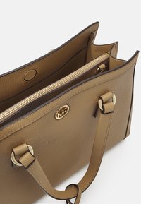 Sac fourre-tout en cuir texturé beige avec quincaillerie dorée. Dispose d'une fermeture éclair en haut et de deux compartiments intérieurs, avec le logo de la marque à l'avant.