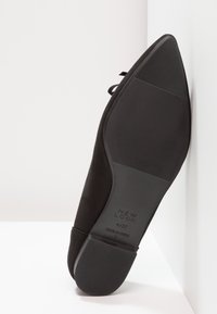 Semelle de chaussure plate noire pointue faisant face en avant, avec une texture antidérapante et un logo "New Look" sur un fond blanc angulaire.