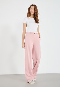 Light pink wide-leg trousers made from smooth fabric, featuring a button closure and side pockets, paired with a fitted white t-shirt.